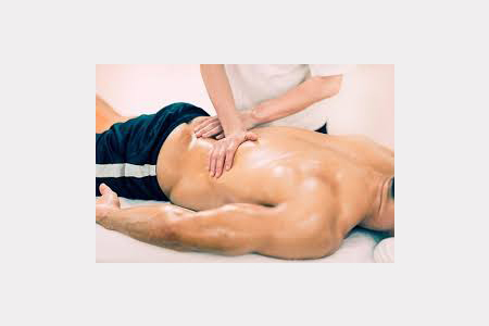 A man lying on his front whilst masseuse massages his lower back 